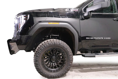 Fab Fours Black Steel front bumper on a black GMC Sierra 2500HD/3500HD, close-up of the front corner, showing diamond-plate end, top tube, wheel-well clearance