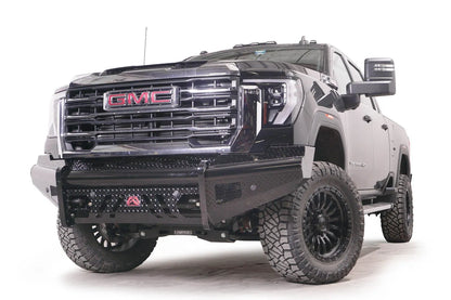 Fab Fours Black Steel front bumper on a black GMC Sierra 2500HD/3500HD, front driver-side three-quarter view, showing diamond-plate finish, top tube, mesh end inserts, Fab Fours badge