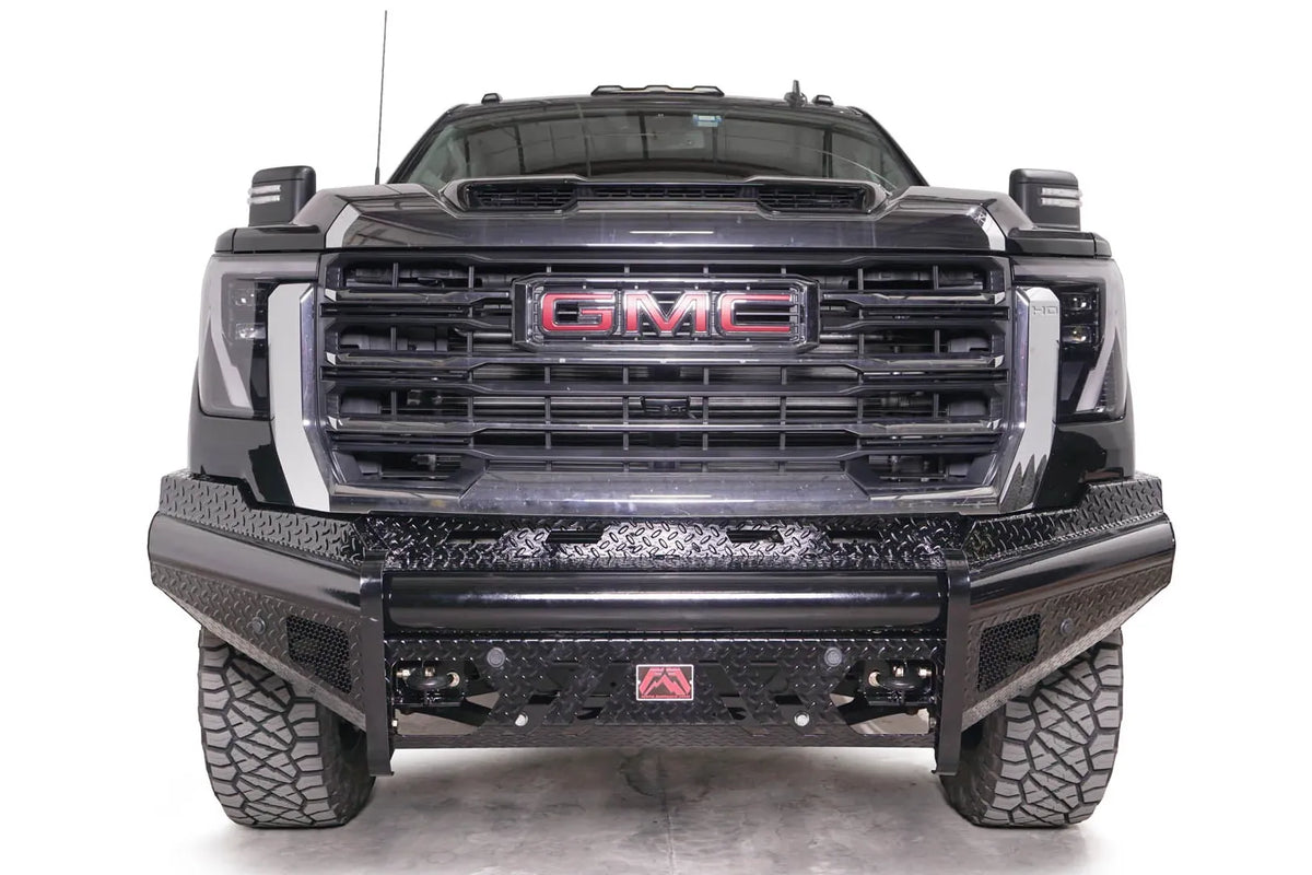 Fab Fours Black Steel front bumper on a black GMC Sierra 2500HD/3500HD, straight-on front view, showing diamond-plate finish, top tube, mesh end inserts, Fab Fours badge