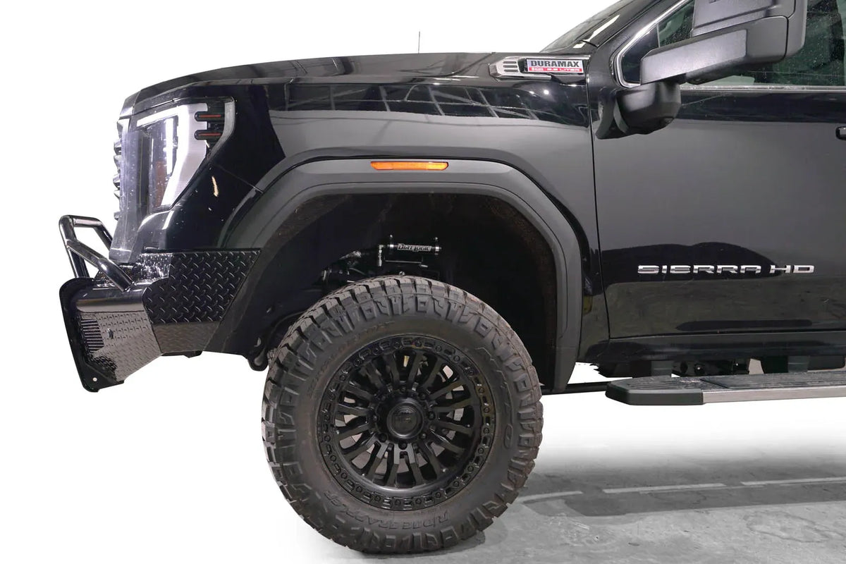 Fab Fours Black Steel front bumper with pre-runner guard on a black GMC Sierra 2500HD/3500HD, close-up of the front corner, showing pre-runner hoop, diamond-plate end, wheel-well clearance