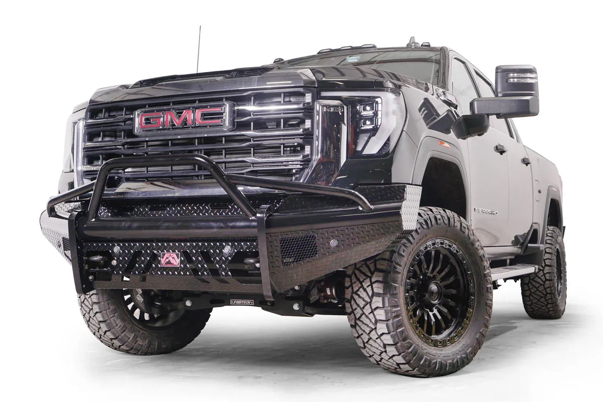 Fab Fours Black Steel front bumper with pre-runner guard on a black GMC Sierra 2500HD/3500HD, front driver-side three-quarter view, showing pre-runner hoop, diamond-plate finish, mesh end inserts, Fab Fours badge