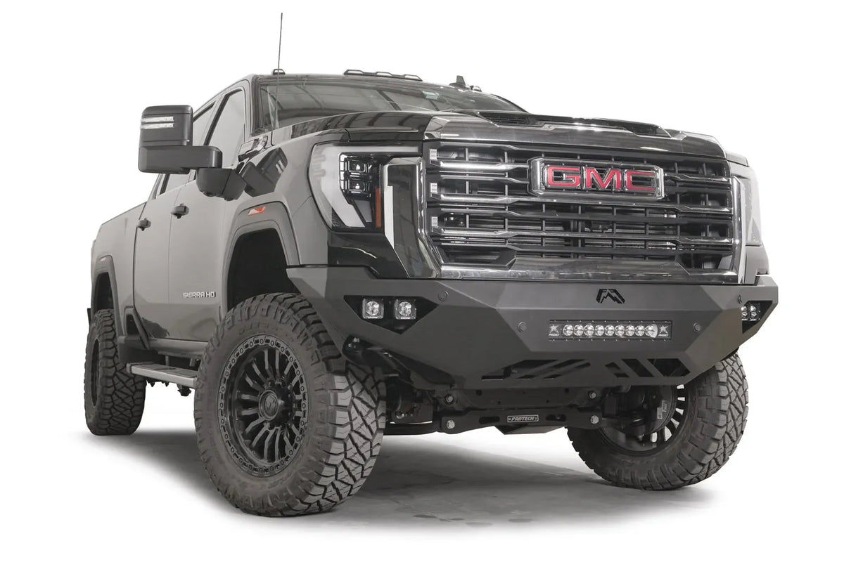 Fab Fours Vengeance front bumper on a black GMC Sierra 2500HD/3500HD, front passenger-side three-quarter view, showing integrated light bar, cube light pods, angular skid plate