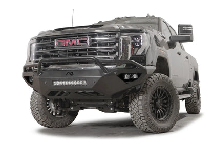 Fab Fours Vengeance front bumper with pre-runner guard on a black GMC Sierra 2500HD/3500HD, front driver-side three-quarter view, showing pre-runner hoop, integrated light bar, cube light pods