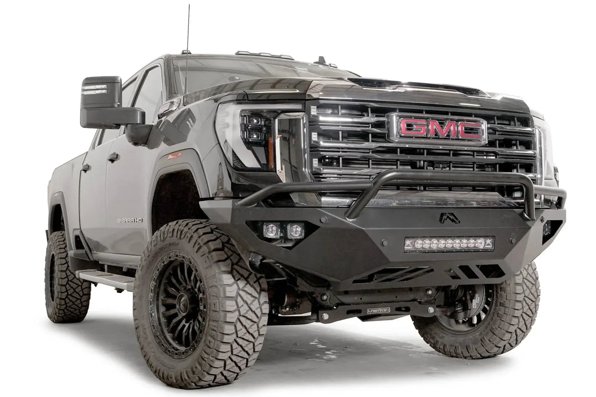 Fab Fours Vengeance front bumper with pre-runner guard on a black GMC Sierra 2500HD/3500HD, front passenger-side three-quarter view, showing pre-runner hoop, integrated light bar, cube light pods