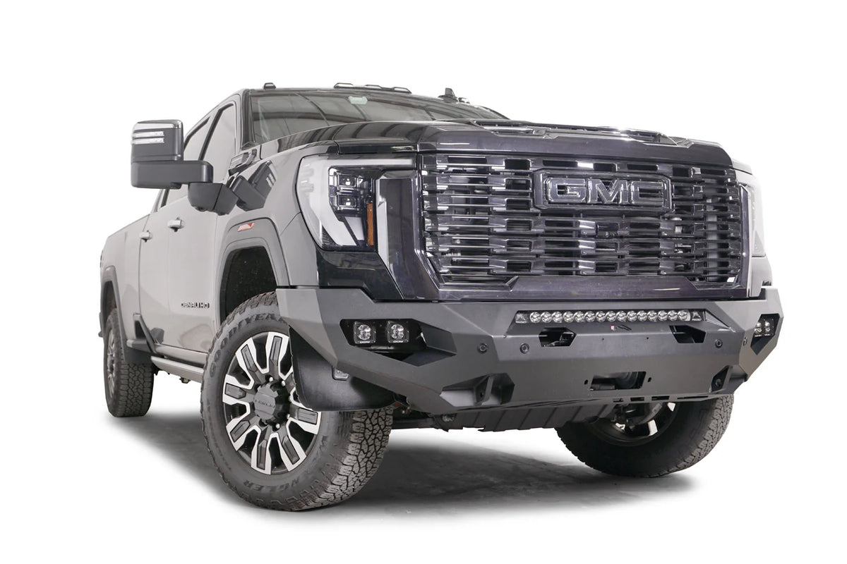 Fab Fours Matrix front bumper on a dark gray GMC Sierra 2500HD/3500HD, front passenger-side three-quarter view, showing integrated light bar, cube light pods, winch-ready center