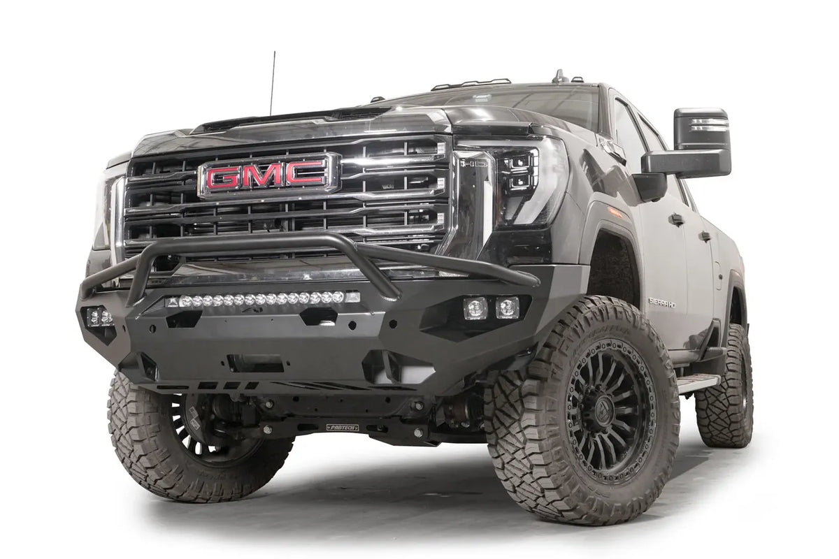 Fab Fours Matrix front bumper with pre-runner guard on a black GMC Sierra 2500HD/3500HD, front driver-side three-quarter view, showing pre-runner hoop, integrated light bar, cube light pods