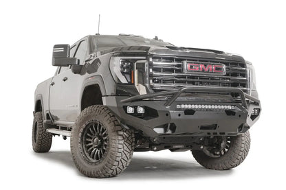 Fab Fours Matrix front bumper with pre-runner guard on a black GMC Sierra 2500HD/3500HD, front passenger-side three-quarter view, showing pre-runner hoop, integrated light bar, cube light pods