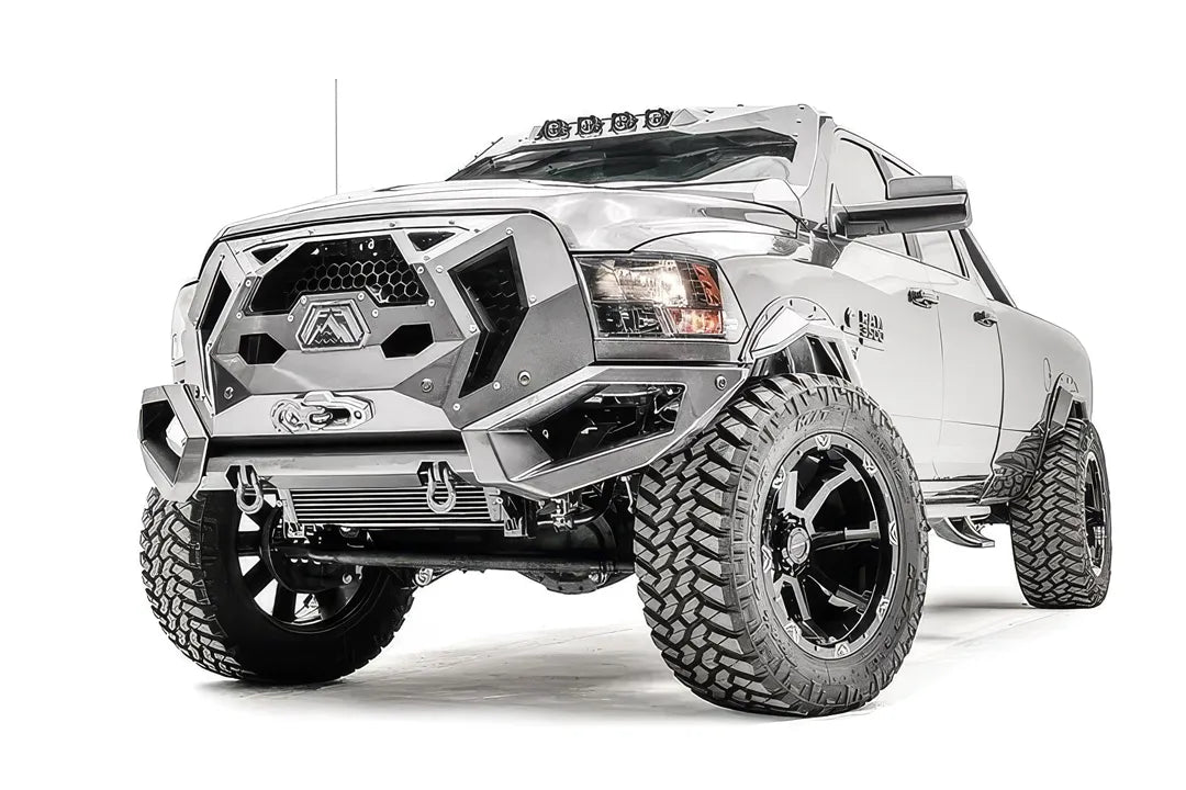 Fab Fours Grumper front bumper with honeycomb mesh grille on a lifted silver Ram 3500, driver-side front three-quarter view, with winch and D-ring shackles