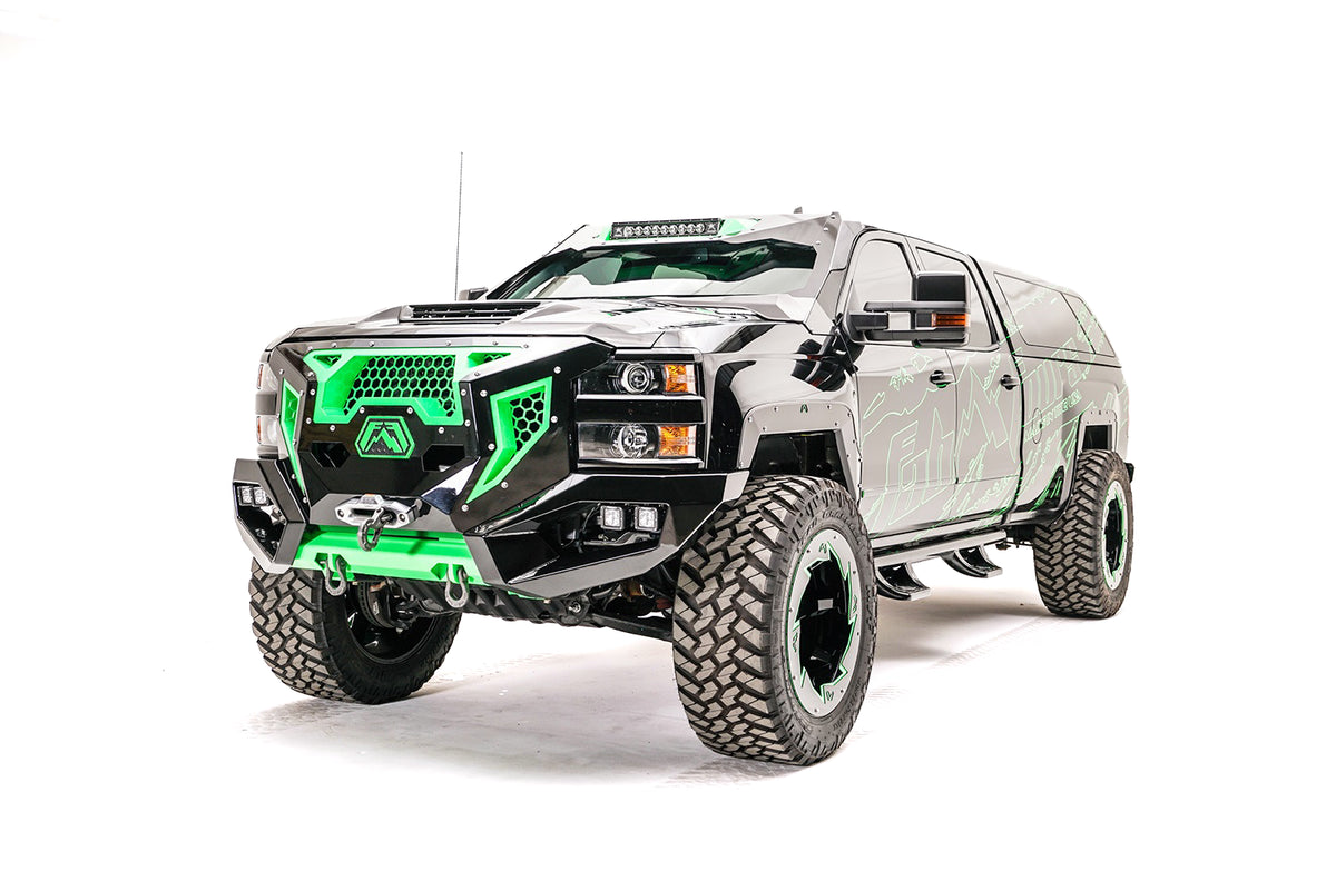 Fab Fours Grumper front bumper with green honeycomb mesh grille on a lifted black Chevrolet Silverado 2500HD with green Fab Fours graphics, driver-side front three-quarter view, with winch and cube lights