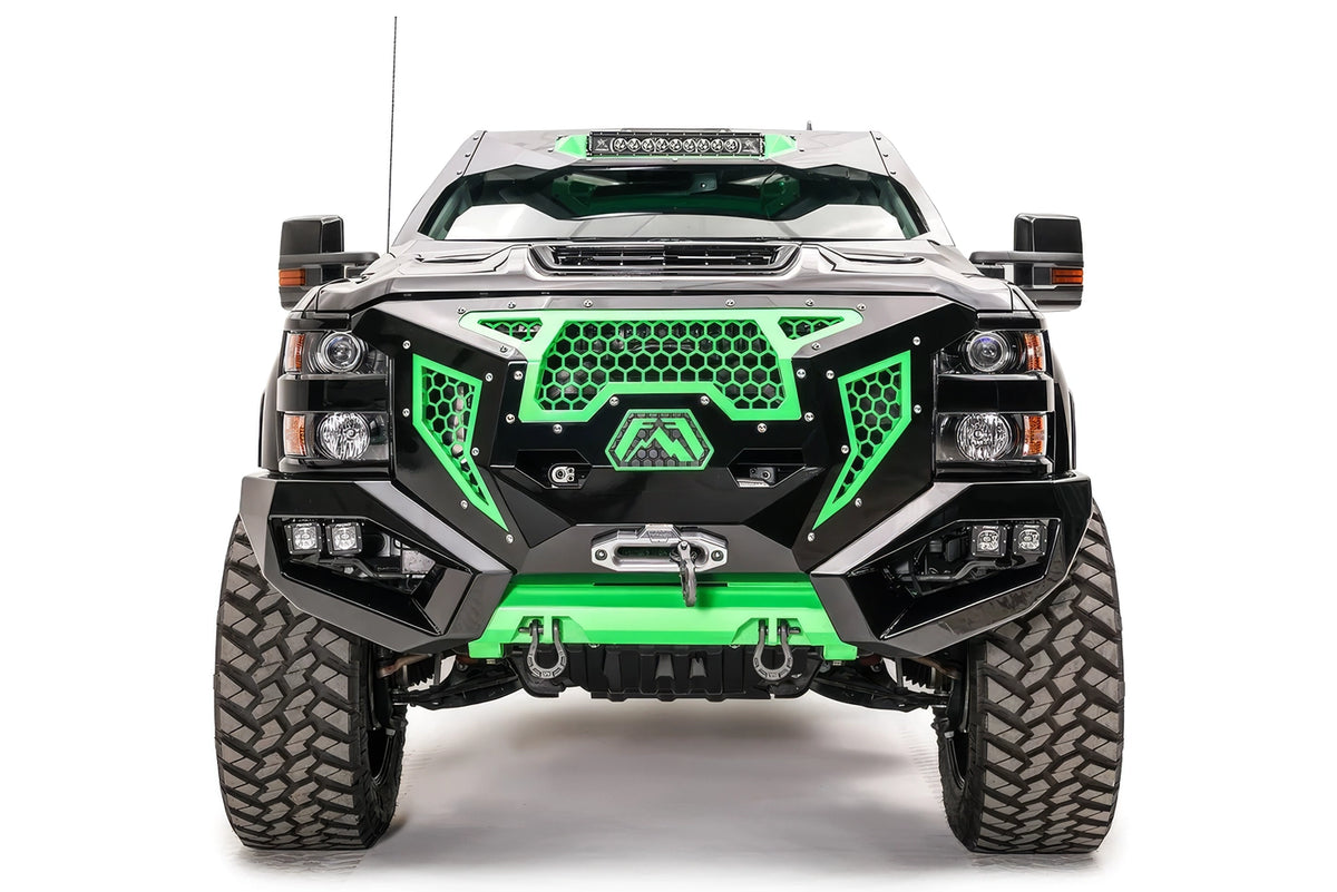 Fab Fours Grumper front bumper on a lifted black Chevrolet Silverado 2500HD, front view, with green honeycomb mesh grille, winch, dual cube lights, D-ring shackles, and green skid plate