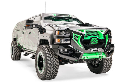 Fab Fours Grumper front bumper with green honeycomb mesh grille on a lifted black Chevrolet Silverado 2500HD with green Fab Fours graphics, passenger-side front three-quarter view, with winch and cube lights