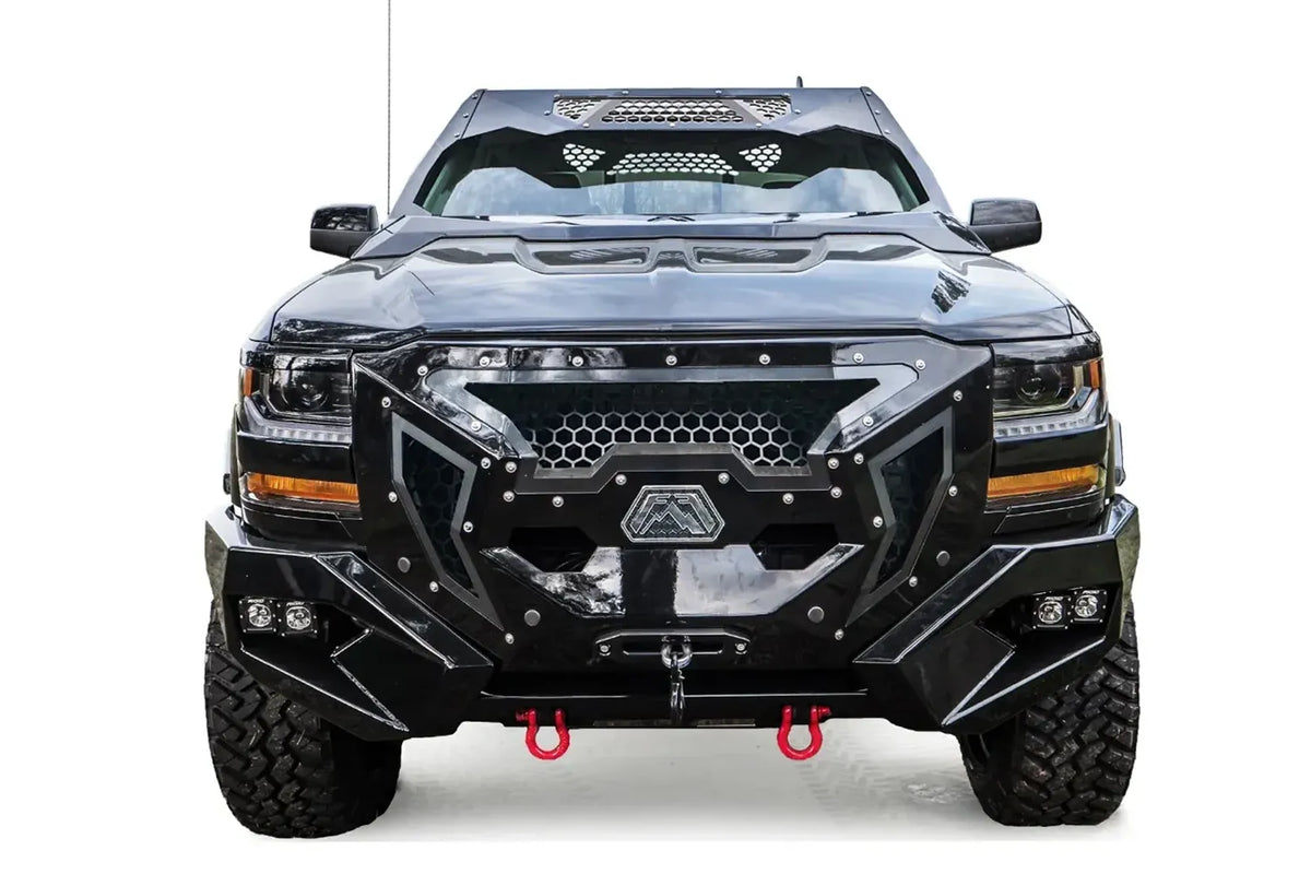 Fab Fours Grumper front winch bumper with full guard on a lifted black 2016–2018 Chevrolet Silverado 1500, straight-on front view, showing the honeycomb mesh grille guard, hexagonal Fab Fours badge, winch with hook, pod lights in the bumper wings and red D-ring shackles