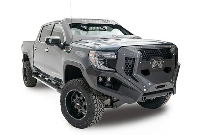 Fab Fours Grumper front bumper and grille with honeycomb mesh on a lifted gray GMC Sierra 1500, passenger-side front three-quarter view, with dual cube lights