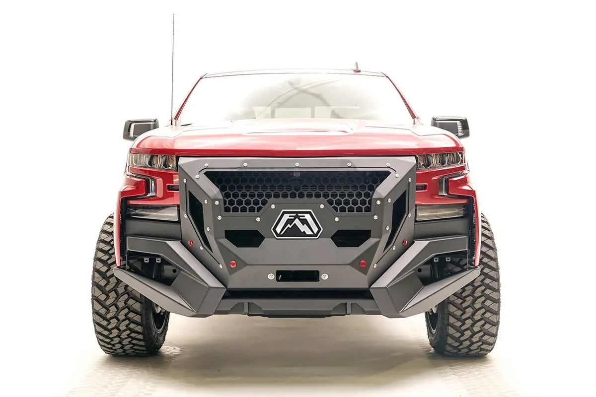 Fab Fours Grumper front winch bumper with full guard on a lifted red 2019–2021 Chevrolet Silverado 1500, straight-on front view, showing the honeycomb mesh grille guard, the hexagonal Fab Fours badge, the winch fairlead opening and the angular bumper wings