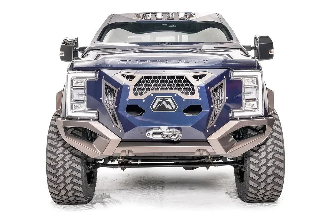 Fab Fours Grumper front bumper on a lifted Ford Super Duty, front view, with blue grille panel, honeycomb mesh, Fab Fours logo plate, and bronze bumper with winch fairlead