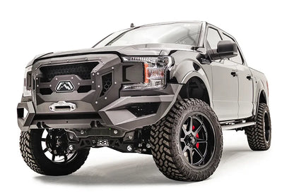Fab Fours Grumper front winch bumper with honeycomb mesh grille on a lifted black Ford F-150, driver-side front three-quarter view, with winch fairlead