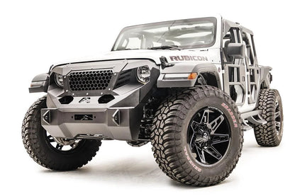 Fab Fours Grumper front winch bumper on a lifted white Jeep Wrangler JL Rubicon, front driver-side view, showing the narrower bumper ends inside the tires, the winch mount, honeycomb mesh grille guard and Fab Fours tube doors