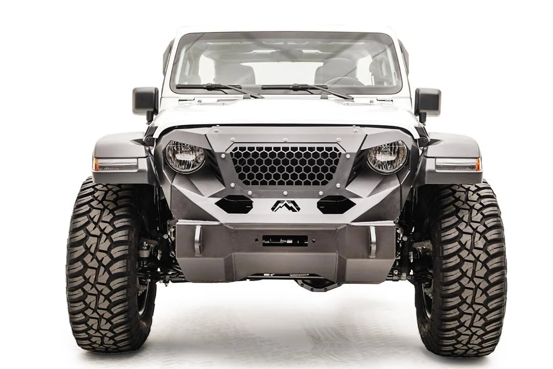 Fab Fours Grumper front winch bumper on a lifted white Jeep Wrangler JL Rubicon, straight-on front view, showing the compact bumper with winch fairlead opening, honeycomb mesh grille guard, Fab Fours logo and D-ring mounts