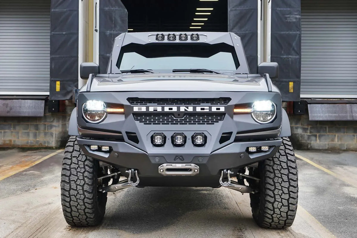 Fab Fours Grumper front bumper on a lifted gray Ford Bronco parked at a loading dock, front view, with three center cube lights and D-ring shackles