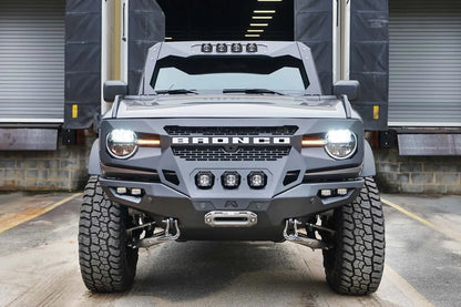 Fab Fours Grumper front bumper on a lifted gray Ford Bronco parked at a loading dock, front view, with three center cube lights and D-ring shackles