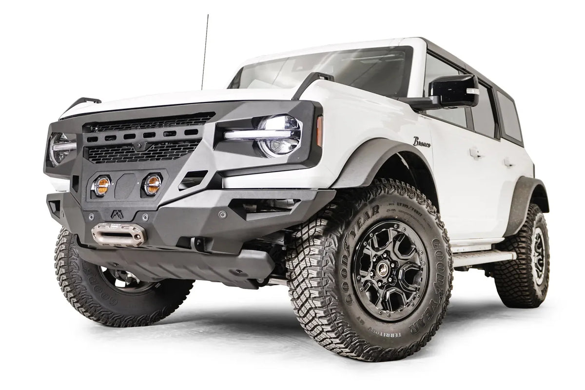 Fab Fours Grumper front bumper with two pod lights on a white Ford Bronco, low driver-side front three-quarter view, with winch fairlead