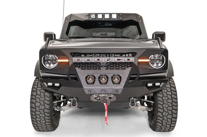 Fab Fours Grumper front bumper on a lifted gray Ford Bronco, front view, with three center pod lights, cube lights, Warn winch, and D-ring shackles