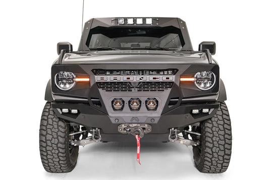 Fab Fours Grumper front bumper on a lifted gray Ford Bronco, front view, with three center pod lights, cube lights, Warn winch, and D-ring shackles