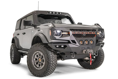 Fab Fours Grumper front bumper with three center pod lights on a lifted gray Ford Bronco, passenger-side front three-quarter view, with Warn winch and D-ring shackles