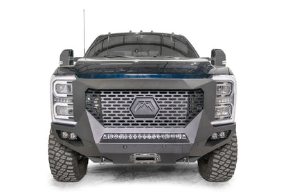 Fab Fours Grumper front winch bumper on a dark blue 2023+ Ford Super Duty, straight-on front view, showing the full-width slotted grille with the hex Fab Fours badge, the center LED light bar, pod lights on each side and the winch fairlead