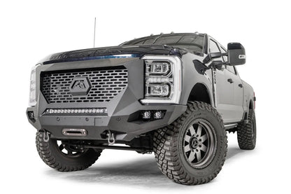Fab Fours Grumper front winch bumper on a lifted dark blue 2023+ Ford Super Duty, front driver-side view, showing the full-height grille guard with the hex Fab Fours logo, the integrated LED light bar, pod lights and a centered winch fairlead with D-ring shackles