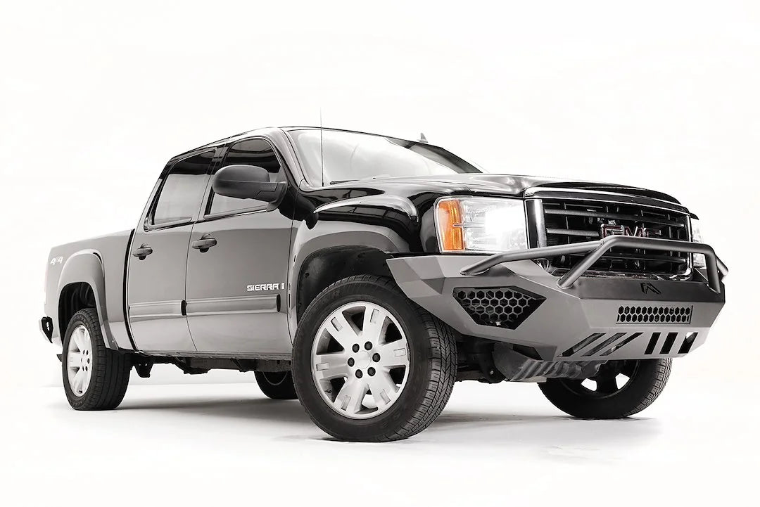 Fab Fours Vengeance front bumper with pre-runner guard on a black and gray GMC Sierra 1500, front passenger-side three-quarter view, showing pre-runner hoop, honeycomb mesh inserts, angular skid plate