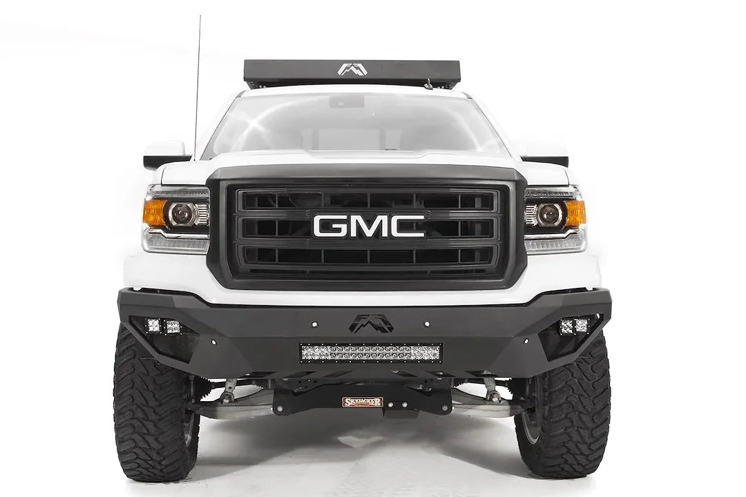 Fab Fours Vengeance front bumper on a white GMC Sierra 1500, straight-on front view, showing integrated light bar, cube light pods, angular skid plate