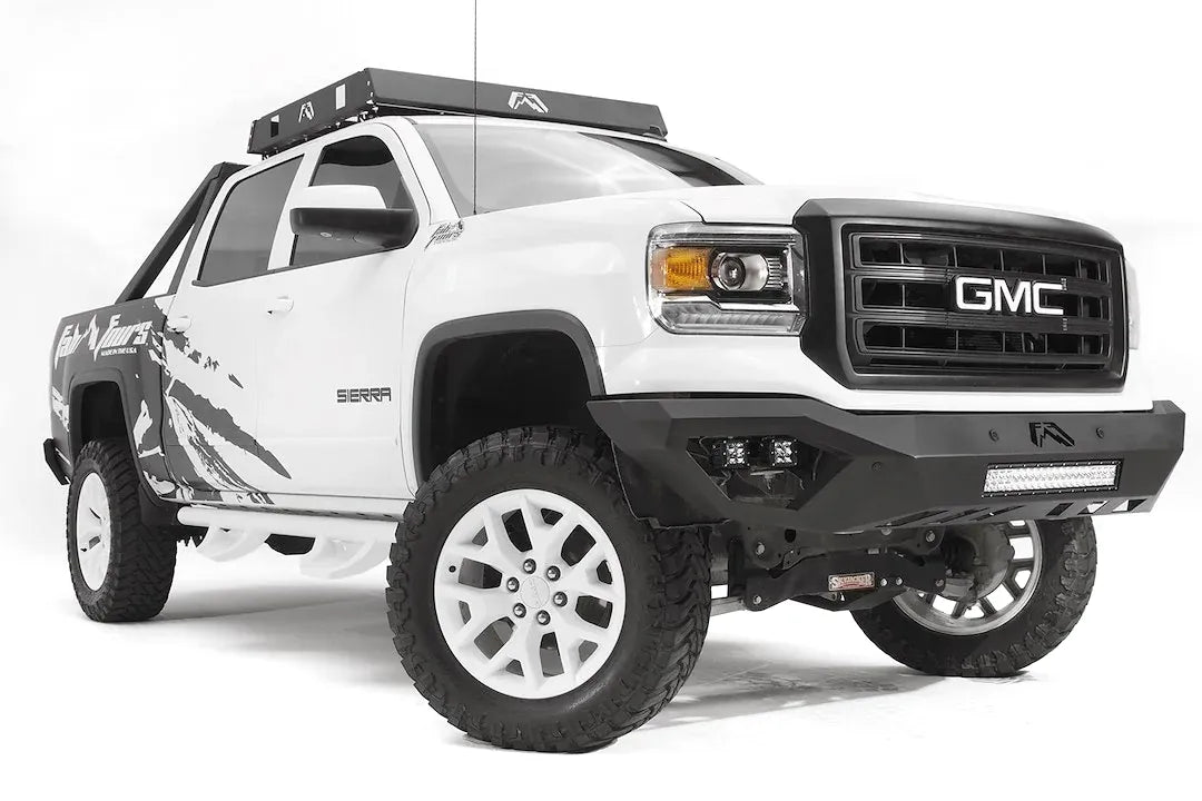 Fab Fours Vengeance front bumper on a white GMC Sierra 1500, front passenger-side three-quarter view, showing integrated light bar, cube light pods, angular skid plate