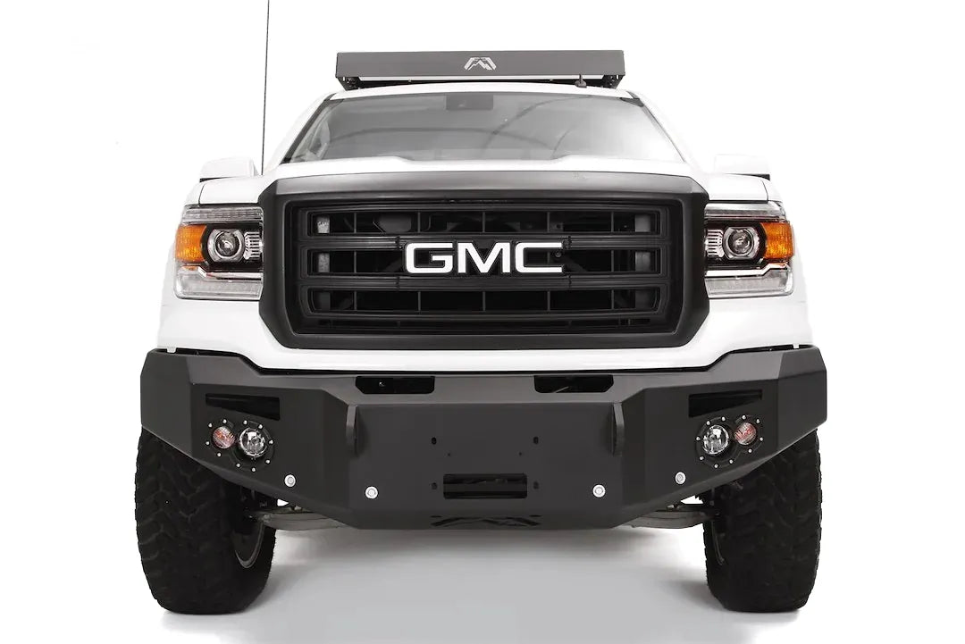 Fab Fours Premium Heavy Duty Winch front bumper on a white GMC Sierra 1500, straight-on front view, showing winch plate, round fog light pods, squared end caps
