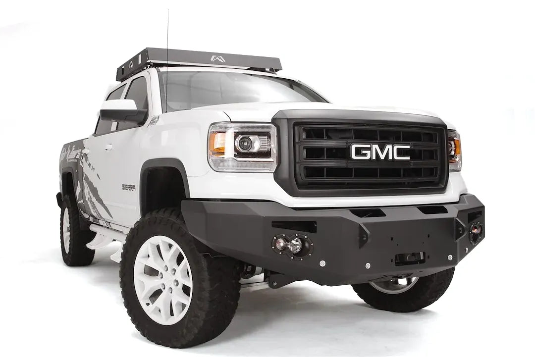 Fab Fours Premium Heavy Duty Winch front bumper on a white GMC Sierra 1500, front passenger-side three-quarter view, showing winch plate, round fog light pods, squared end caps