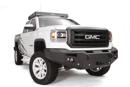 Fab Fours Premium Heavy Duty Winch front bumper on a white GMC Sierra 1500, front passenger-side three-quarter view, showing winch plate, round fog light pods, squared end caps