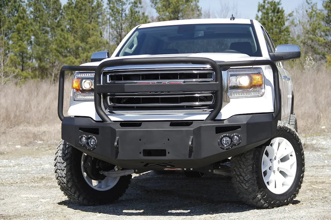 Fab Fours Premium Winch front bumper with full guard on a white GMC Sierra 1500, straight-on front view outdoors, showing full guard hoop, winch plate, round fog light pods