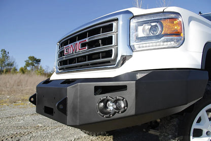 Fab Fours Premium Winch front bumper on a white GMC Sierra 1500, close-up of the bumper outdoors, showing fog light pod, winch opening, squared end cap
