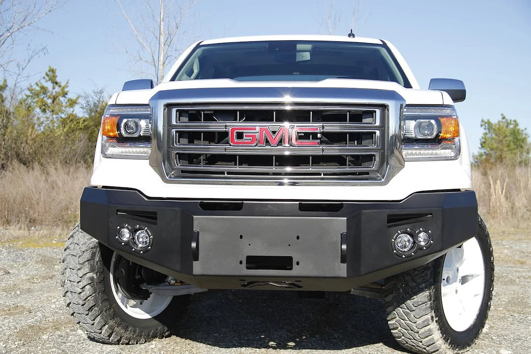 Fab Fours Premium Winch front bumper on a white GMC Sierra 1500, straight-on front view outdoors, showing winch plate, round fog light pods, squared end caps