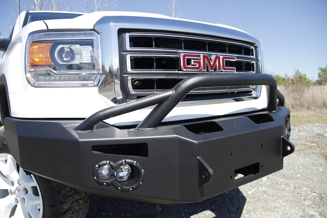 Fab Fours Premium Winch front bumper with pre-runner guard on a white GMC Sierra 1500, close-up of the bumper outdoors, showing pre-runner hoop, fog light pod, winch opening