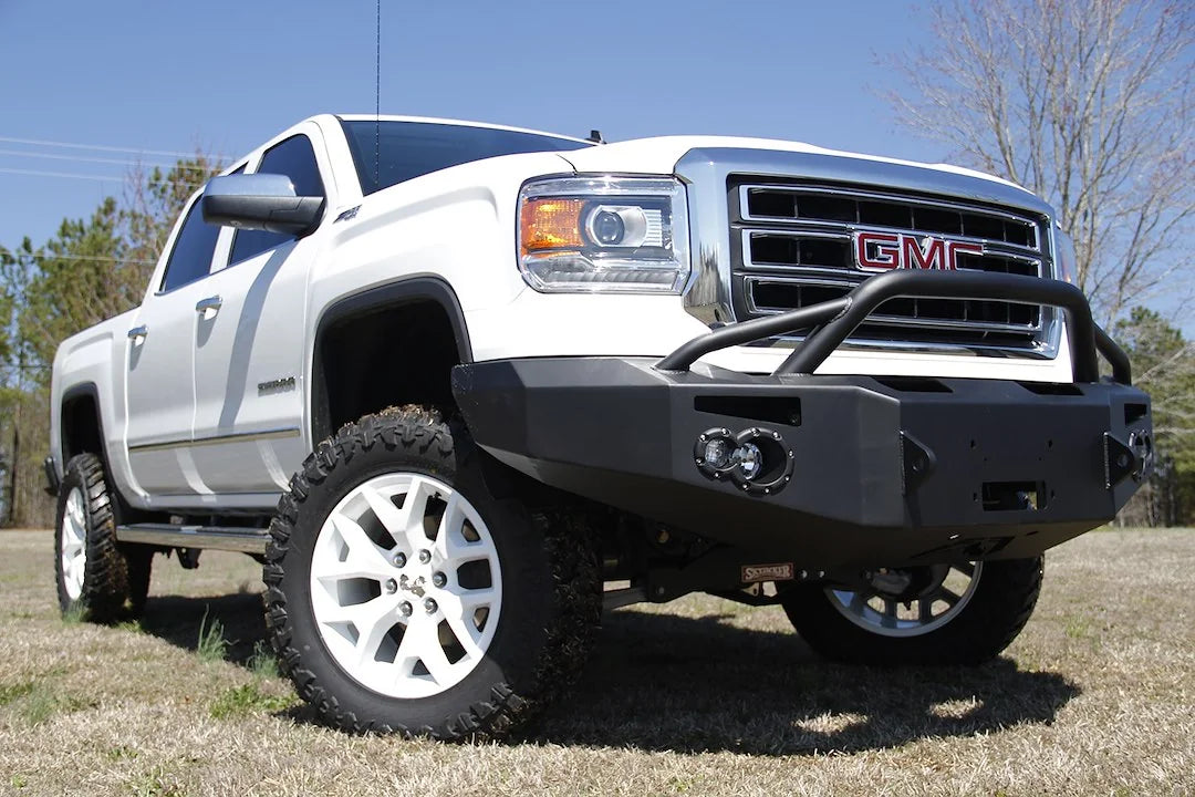Fab Fours Premium Winch front bumper with pre-runner guard on a white GMC Sierra 1500, straight-on front view, showing pre-runner hoop, winch plate, round fog light pods