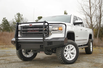 Fab Fours Black Steel front bumper with full guard on a white GMC Sierra 1500, driver-side front three-quarter view outdoors, showing the full grille guard, diamond-plate bumper face and integrated light openings