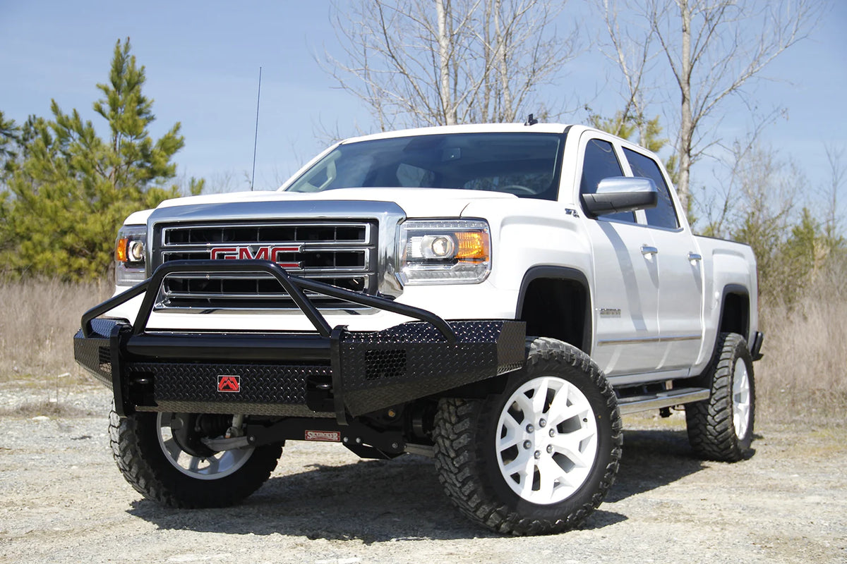 Fab Fours Black Steel front bumper with pre-runner guard on a white GMC Sierra 1500, driver-side front three-quarter view outdoors, showing the pre-runner hoop, diamond-plate bumper face and wrapped end caps