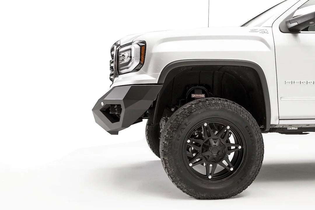 Fab Fours Vengeance front bumper on a white GMC Sierra 1500, close-up of the front corner, showing the angled end cap and wheel clearance