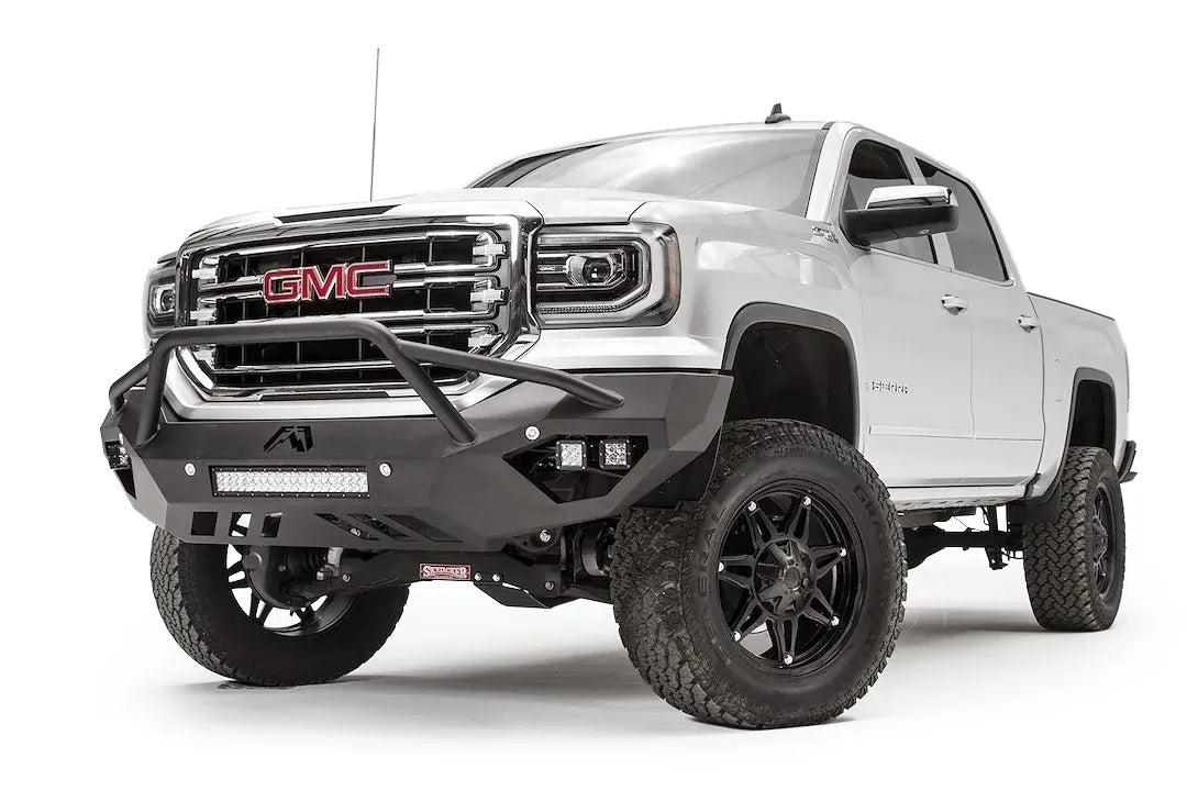 Fab Fours Vengeance front bumper with pre-runner guard on a white GMC Sierra 1500, driver-side front three-quarter view, showing the pre-runner hoop, pod light cutouts and lower light bar mount