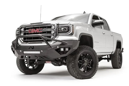 Fab Fours Vengeance front bumper with pre-runner guard on a white GMC Sierra 1500, driver-side front three-quarter view, showing the pre-runner hoop, pod light cutouts and lower light bar mount