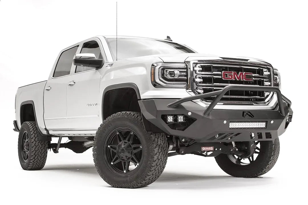 Fab Fours Vengeance front bumper with pre-runner guard on a white GMC Sierra 1500, passenger-side front three-quarter view, showing the pre-runner hoop, pod light cutouts and lower light bar mount