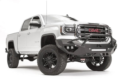 Fab Fours Vengeance front bumper with pre-runner guard on a white GMC Sierra 1500, passenger-side front three-quarter view, showing the pre-runner hoop, pod light cutouts and lower light bar mount