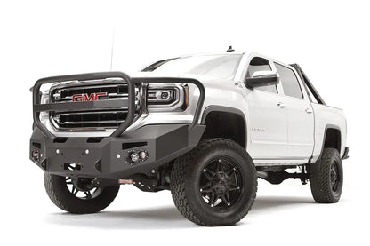 Fab Fours Premium Winch front bumper with full guard on a white GMC Sierra 1500, driver-side front three-quarter view, showing the full grille guard, winch fairlead opening and round fog lights