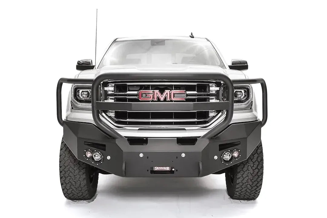 Fab Fours Premium Winch front bumper with full guard on a white GMC Sierra 1500, straight-on front view, showing the full grille guard with headlight hoops, winch fairlead opening and round fog lights